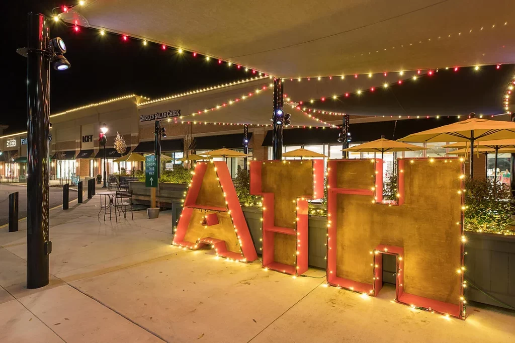 Outdoor shopping area with illuminated oversized letters at night.