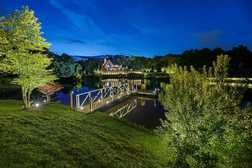 Illuminated lakeside house at twilight with dock and trees.