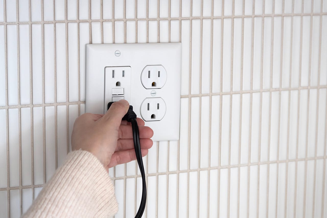 Hand plugging into wall outlet.